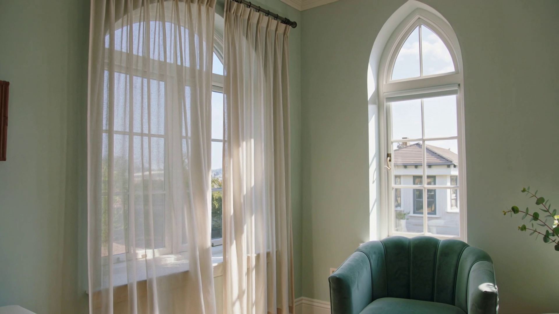 A calm lounge with sage armchairs, a candle and sheer curtains